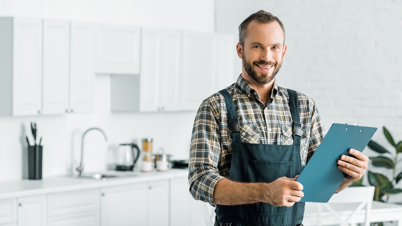 Smiling man in work overalls holding blue clipboard in modern kitchen
