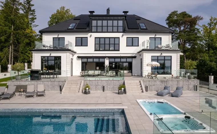 Modern white house with a heat pump mounted on the exterior wall and a patio with chairs and table